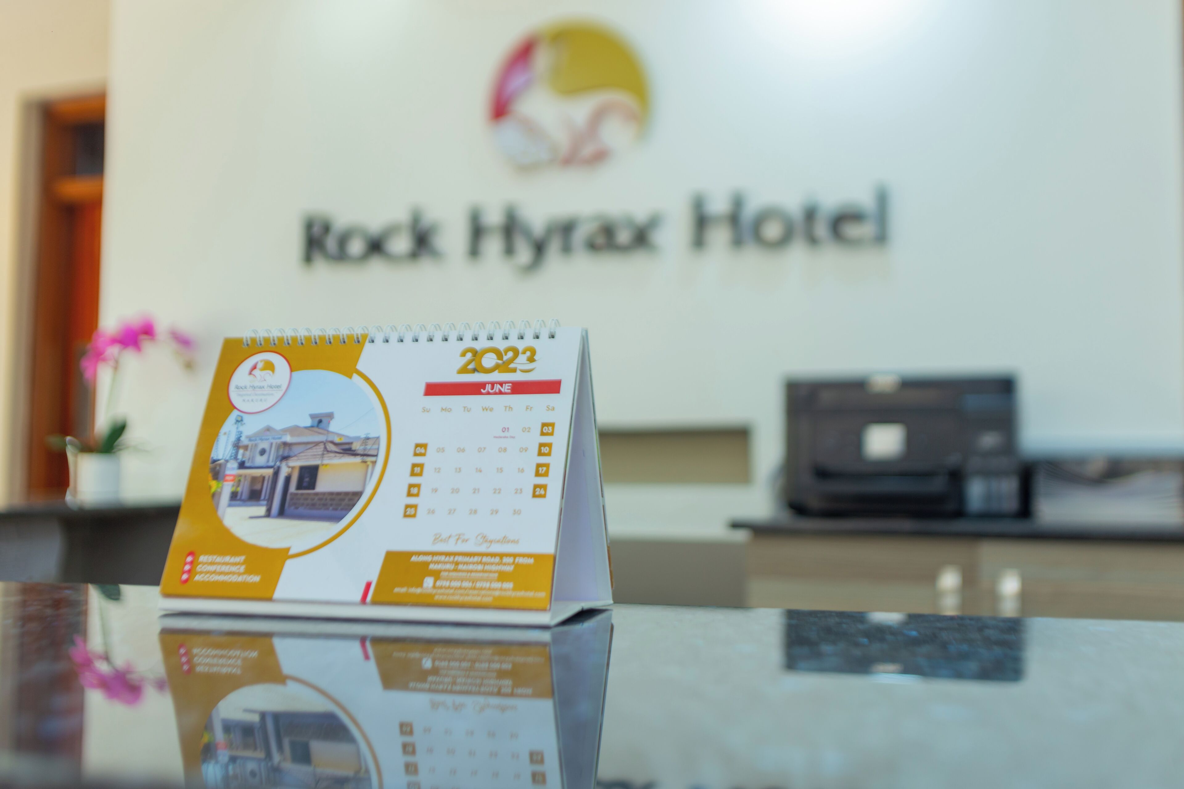 Un mostrador de recepción de hotel con un calendario para junio de 2023, un área de recepción y un logotipo en la pared.