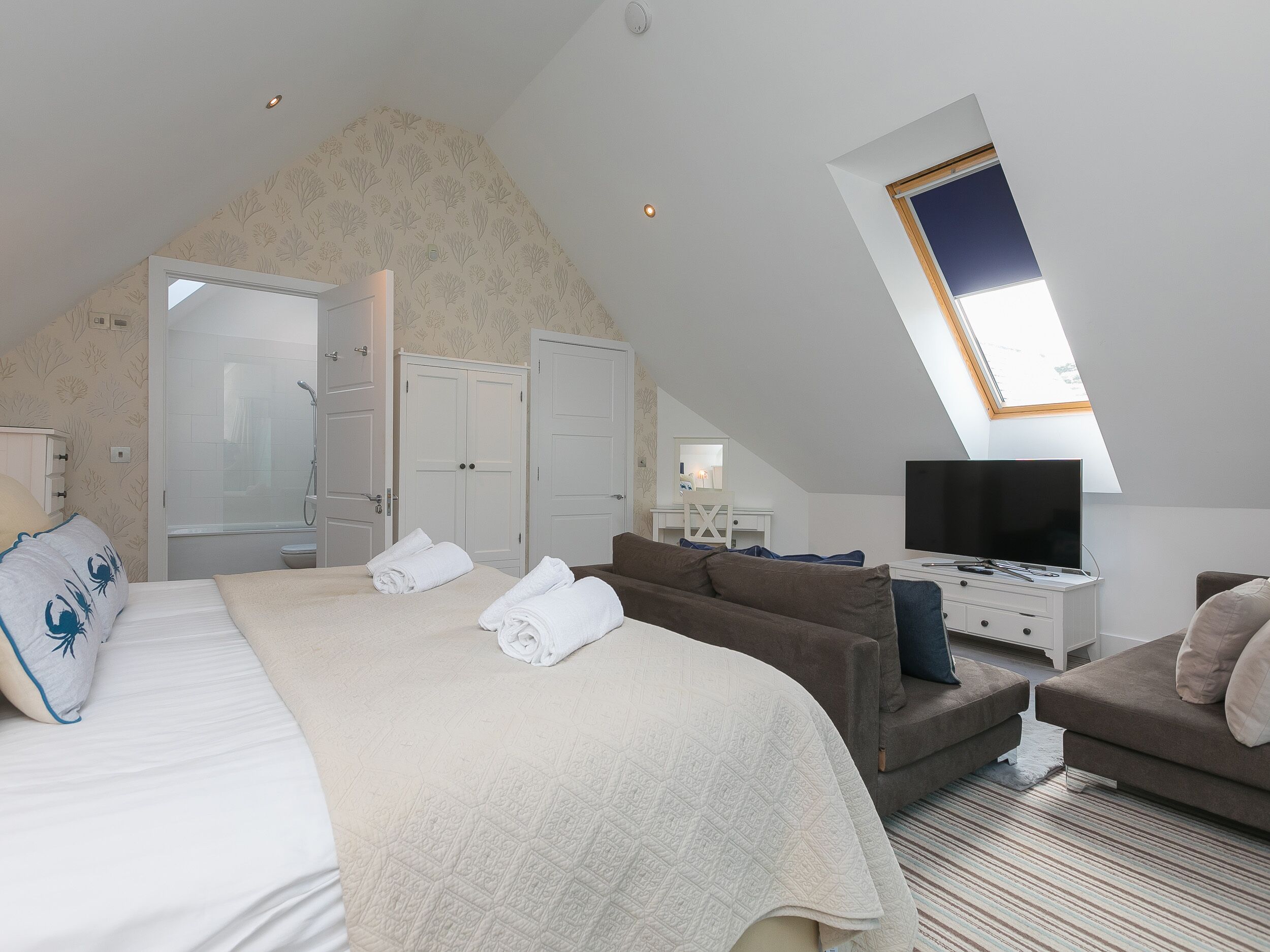 Ein Schlafzimmer mit einem großen Bett, einer Couch, einem Fernseher und einem Oberlicht.