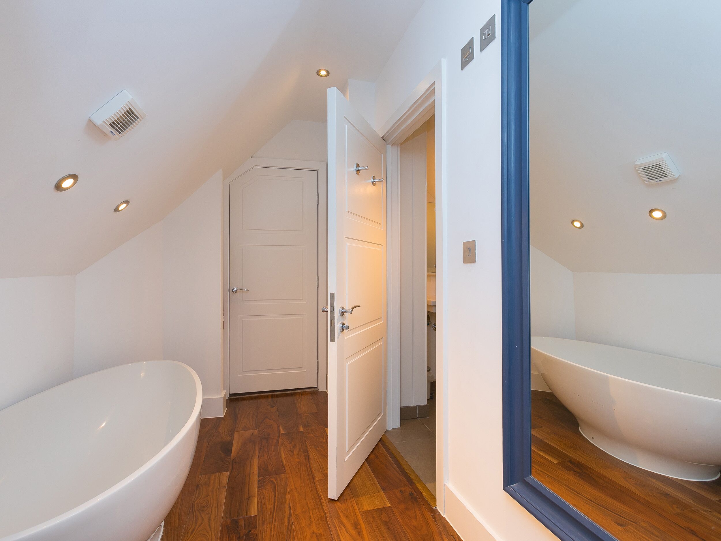 A modern bathroom with a freestanding bathtub, a shower area, and a door leading to another room.