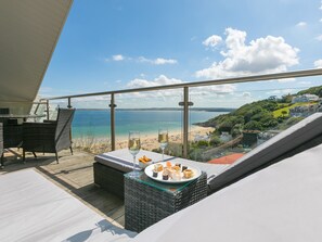 A balcony with a view of the beach and ocean, wicker furniture, and a glass table with food and drinks. - Porthminster Penthouse (St Ives)