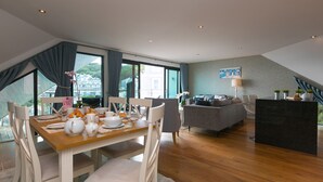 A modern living room with a dining area, a grey sofa, and a view of the outside. - Porthminster Penthouse (St Ives)