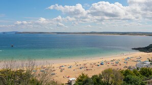 A beach with tents and umbrellas, a clear sky, and calm waters. - Porthminster Penthouse (St Ives)