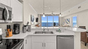 Une cuisine moderne dotée d’un grand îlot central, d’appareils électroménagers en acier inoxydable et offrant une vue sur l’océan.