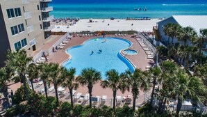 Un hôtel doté d’une grande piscine entourée de palmiers et de chaises longues, offrant une vue sur une plage et l’océan.