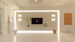A modern living room with a flat-screen TV mounted on a white wall, a minimalist console table, and a large woven rug on the floor. - Blue Sky Villa in Crete (Hersonissos)