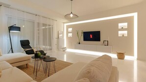 A modern living room with a white sofa, a black chair, a coffee table, and a TV mounted on the wall. - Blue Sky Villa in Crete (Hersonissos)