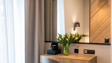 A modern hotel room with a wooden desk, a coffee machine, a vase with tulips, and a mirror with a wooden panel design.