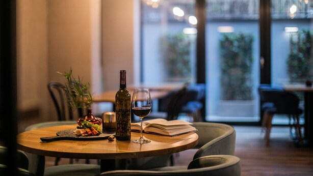 A round wooden table with a bottle of wine, a glass of wine, and a plate of food. - Hotel Vesper House (Gdansk)