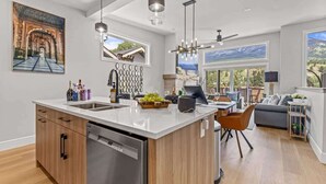A modern kitchen with a central island, a dining area with a sofa, and large windows offering a mountain view. - BRAND NEW|Vienna by SSR|TopView|Luxury|PRIVATE HOT TUB|4BR ( BL# RES-11679 ) (Canmore)