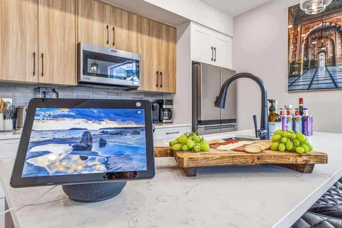 A modern kitchen with wooden cabinets, stainless steel appliances, and a wooden cutting board with grapes and cheese.