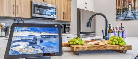 A modern kitchen with wooden cabinets, stainless steel appliances, and a wooden cutting board with grapes and cheese.
