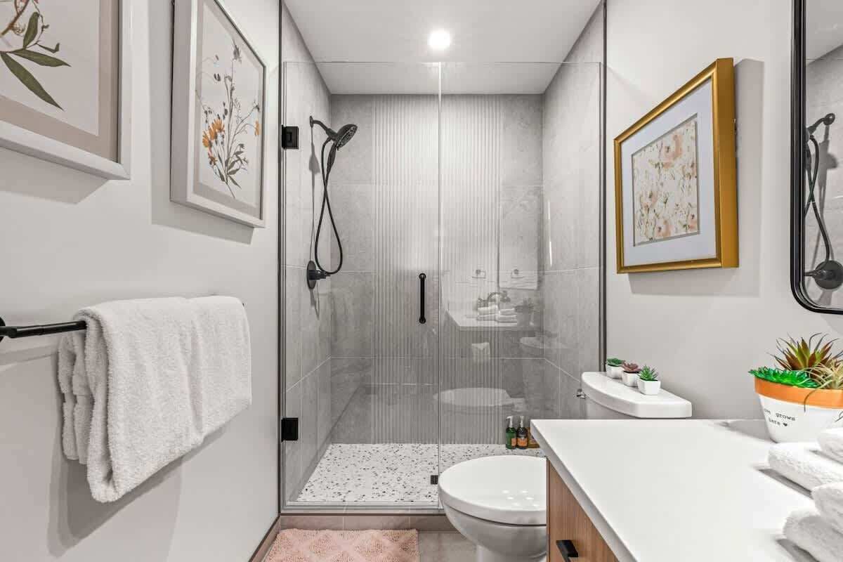 Un baño moderno con ducha envuelta en vidrio, inodoro y lavamanos con encimera.