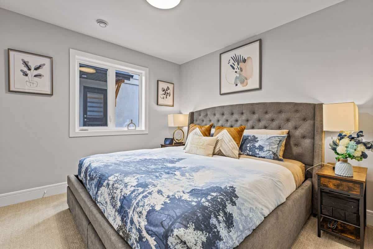A bedroom with a large bed, a nightstand, a window, and framed artwork on the walls.