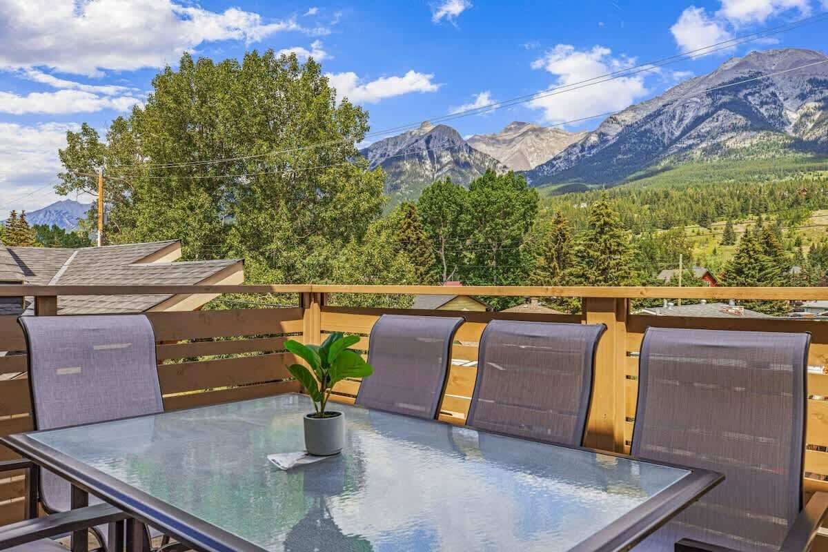 An outdoor seating area with a glass table and chairs, a potted plant, and a view of mountains.