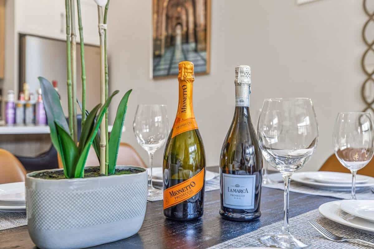 Ein Esstisch mit zwei Prosecco-Flaschen, einer Topfpflanze und leeren Weinkästen.