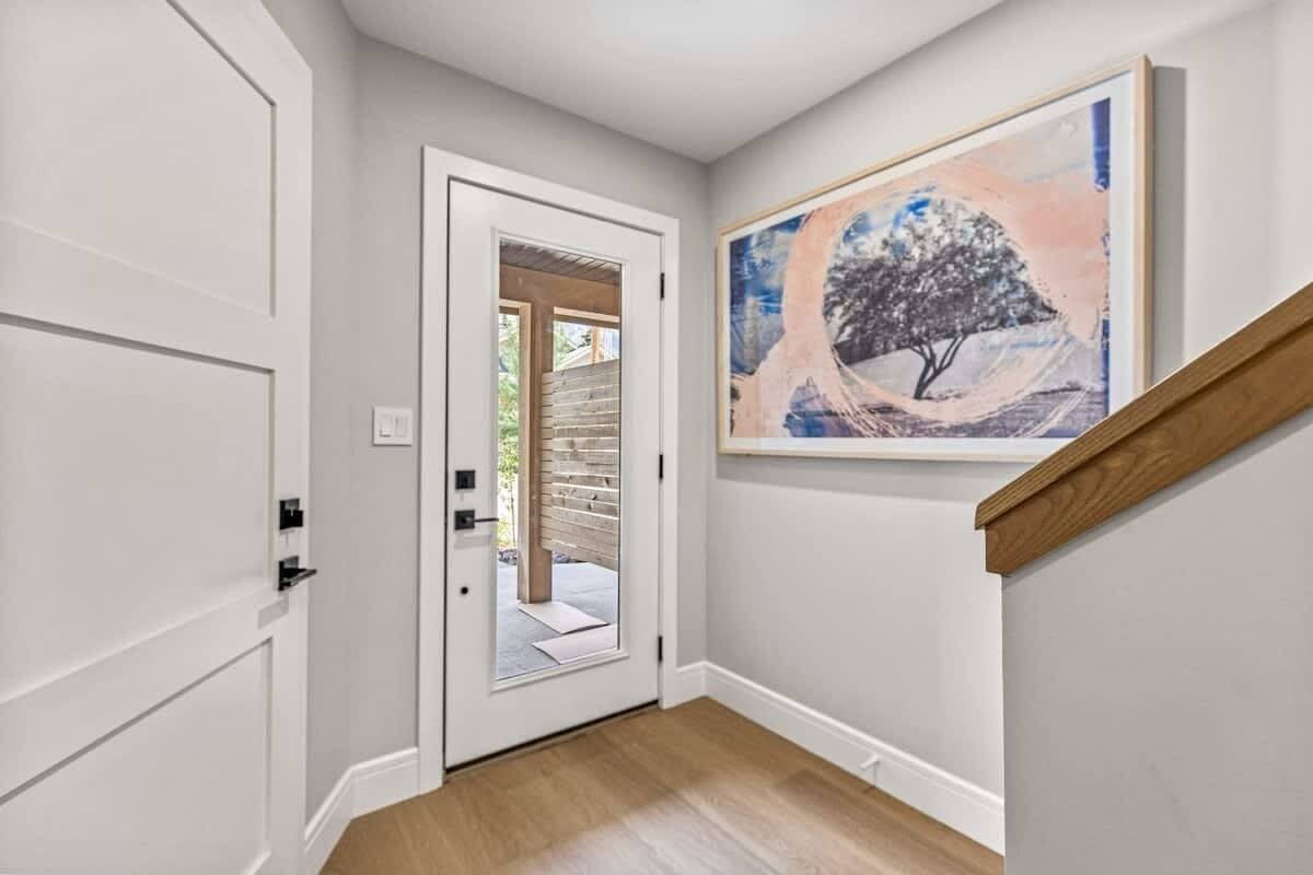 Un couloir avec un plancher en bois, une porte blanche et un tableau représentant un arbre accroché au mur.
