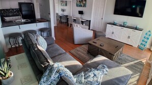 Una sala de estar moderna con un sofá, una mesa de centro y un televisor. Hay una zona de cocina con un refrigerador y una mesa de comedor.