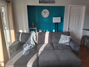 A living room with a sofa, a clock, a lamp, and a door.