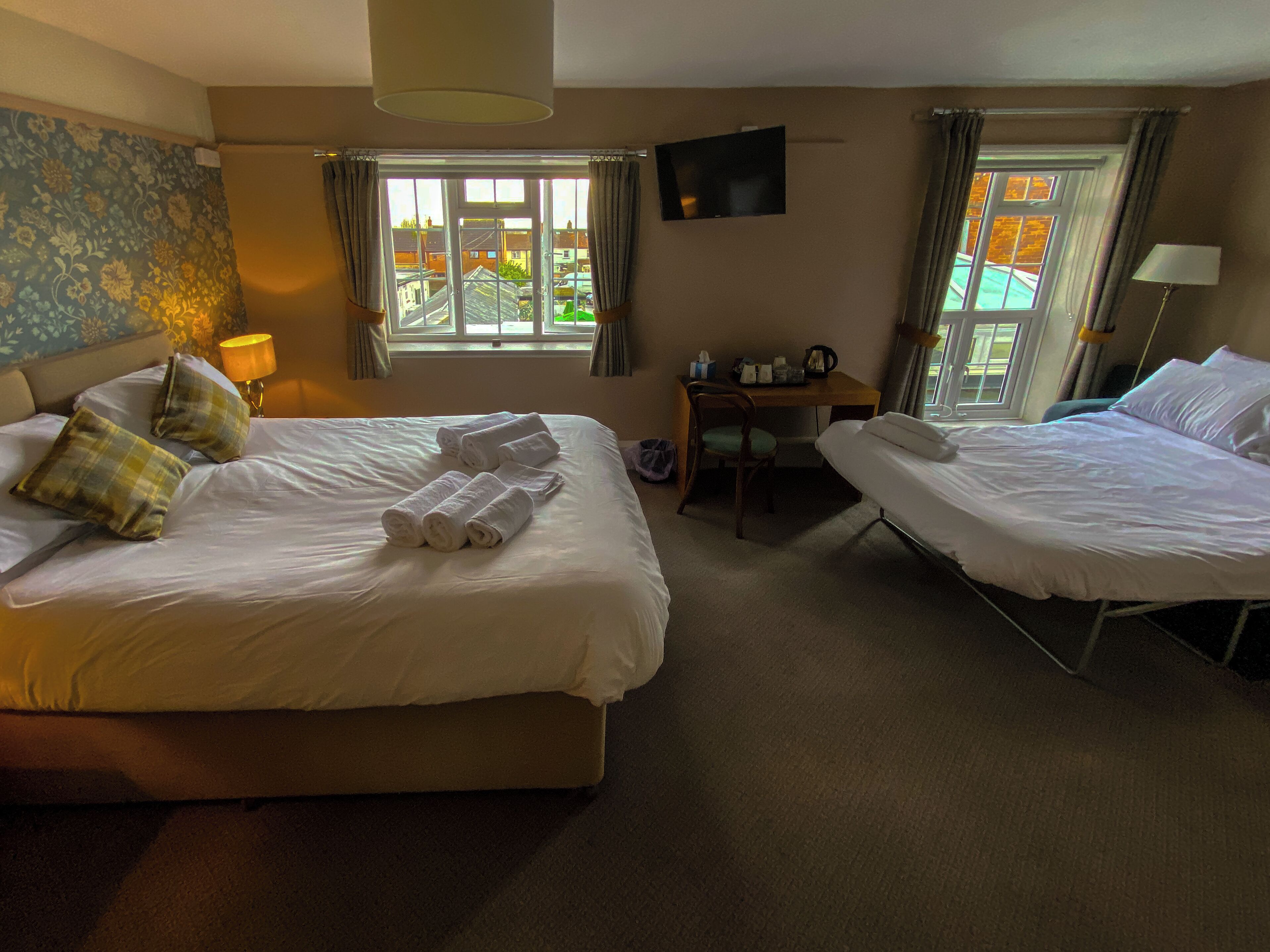 Habitación de hotel con dos camas, un escritorio, una silla, un televisor y una ventana con cortinas.