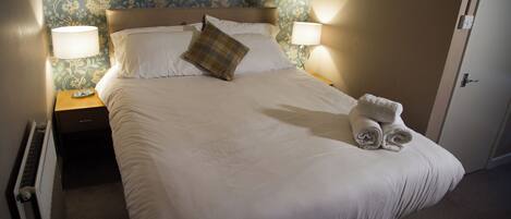 A neatly made bed with white linens and a plaid pillow, flanked by two bedside lamps.