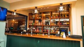 A bar with wooden shelves stocked with various bottles, a cash register, and a digital screen. - Market House (Glastonbury)