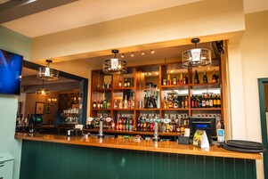 Un bar con estantes de madera llenos de diversas botellas, una caja registradora y una pantalla digital.