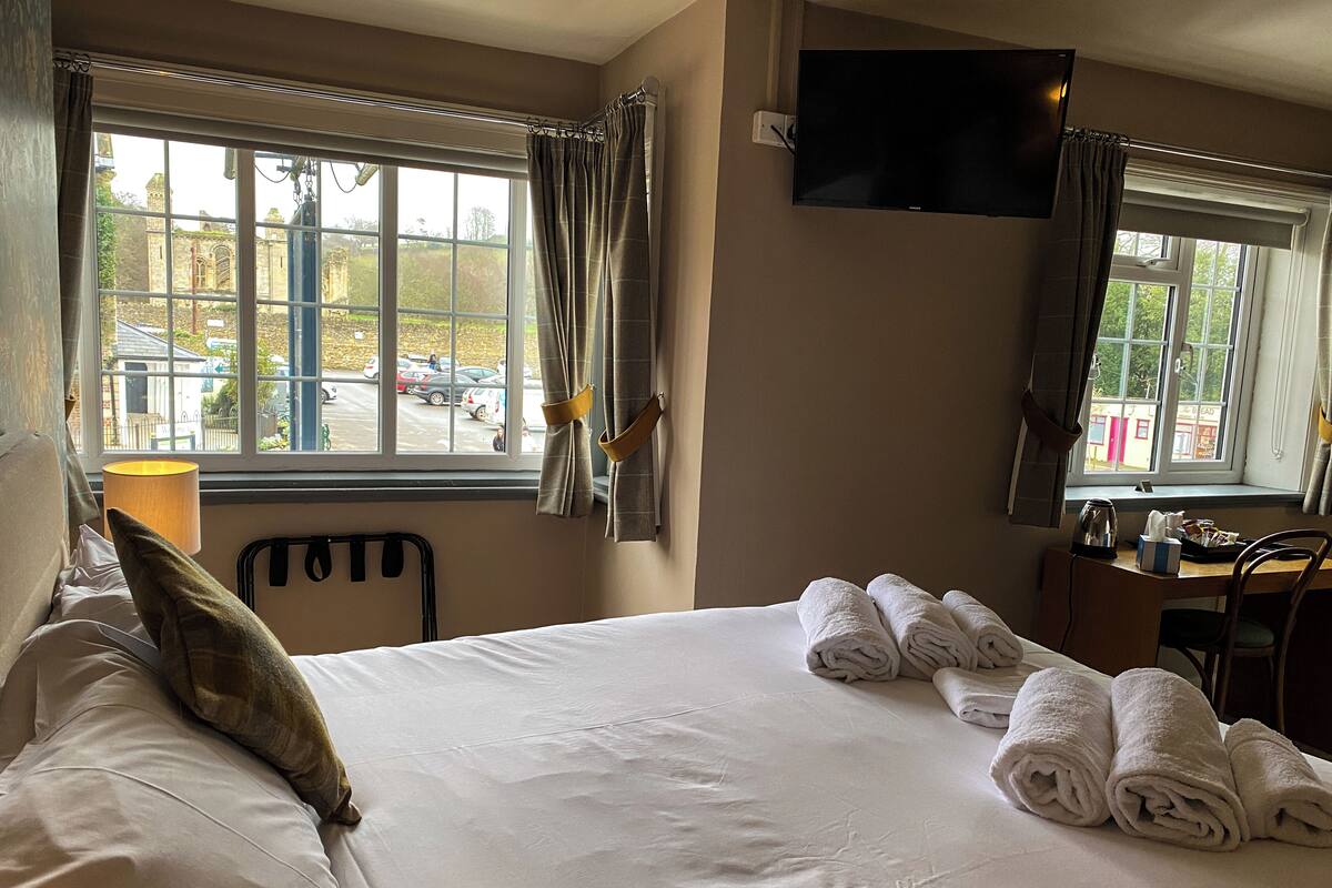 A hotel room with a large bed, a desk, a chair, a TV, and a window with curtains.