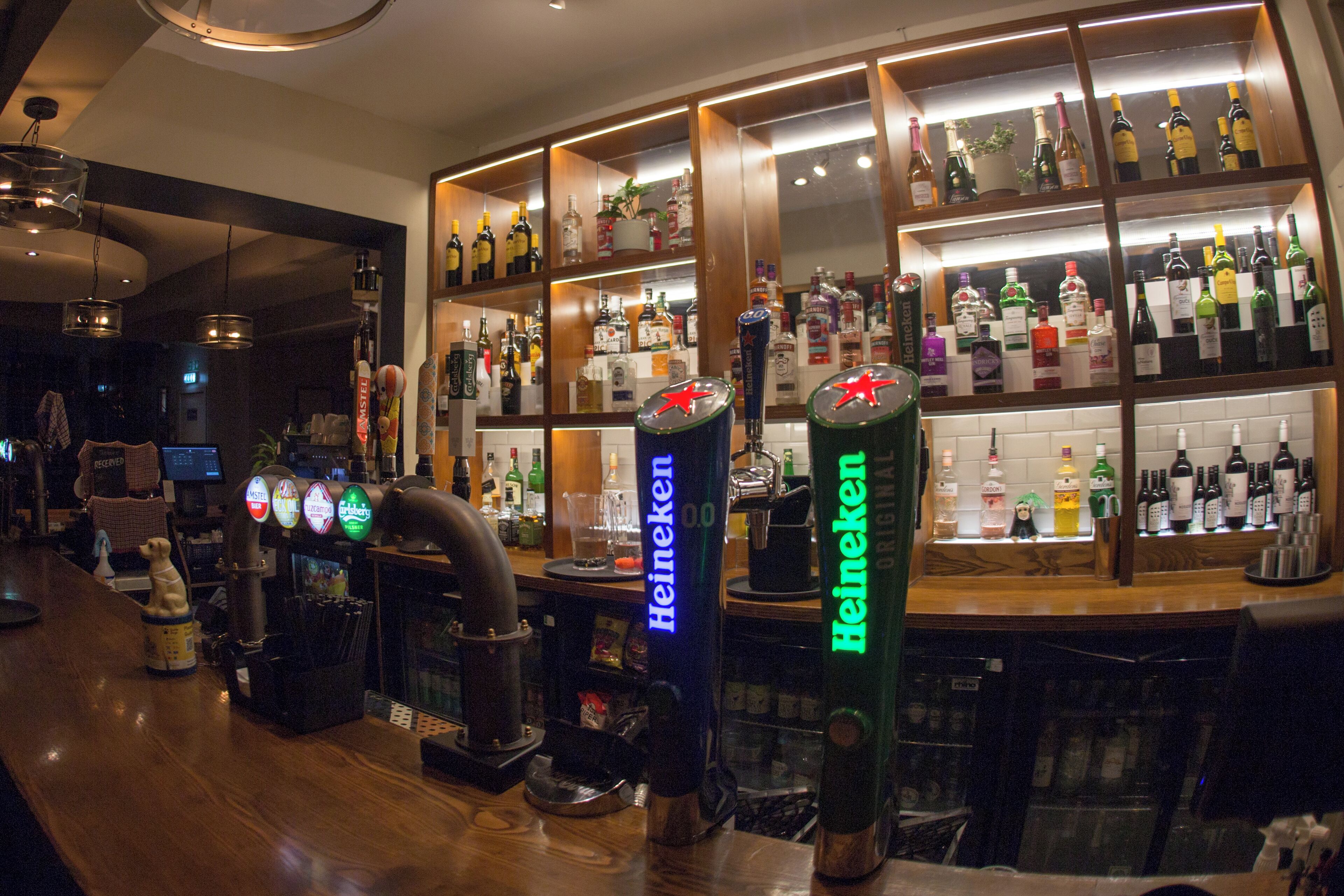 A bar area with multiple Heineken beer taps and a variety of liquor bottles on shelves.