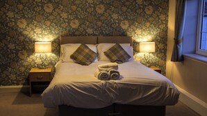 A neatly made bed with two pillows, a bedside lamp, and a rolled towel on the bed. - Market House (Glastonbury)