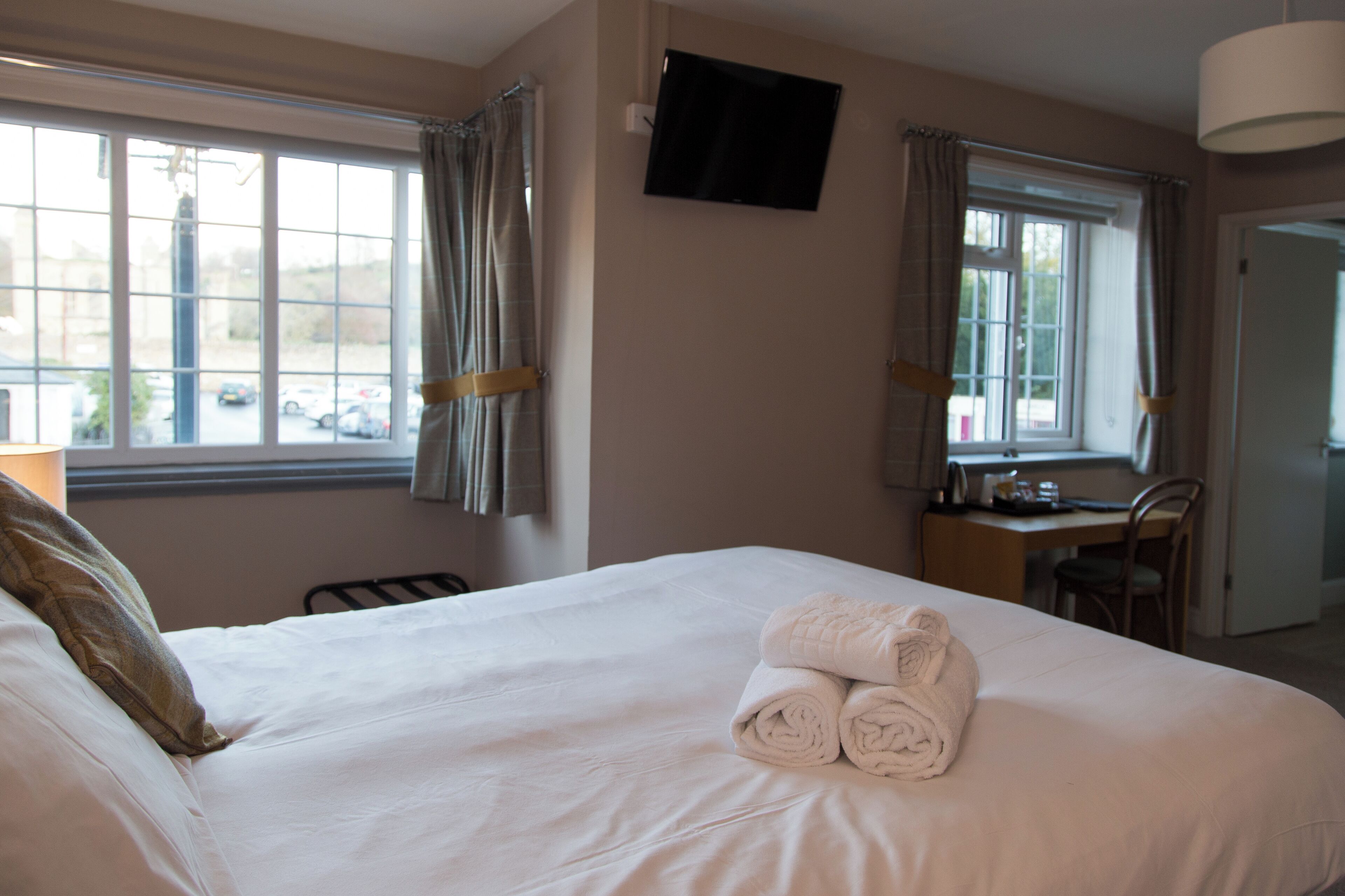 A hotel room with a large bed, two windows with curtains, a desk, and a television on the wall.