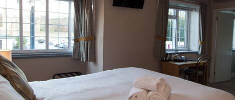 A hotel room with a large bed, two windows with curtains, a desk, and a television on the wall.