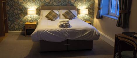A neatly made bed with pillows and a rolled towel, two bedside lamps, a wooden nightstand, and a chair.