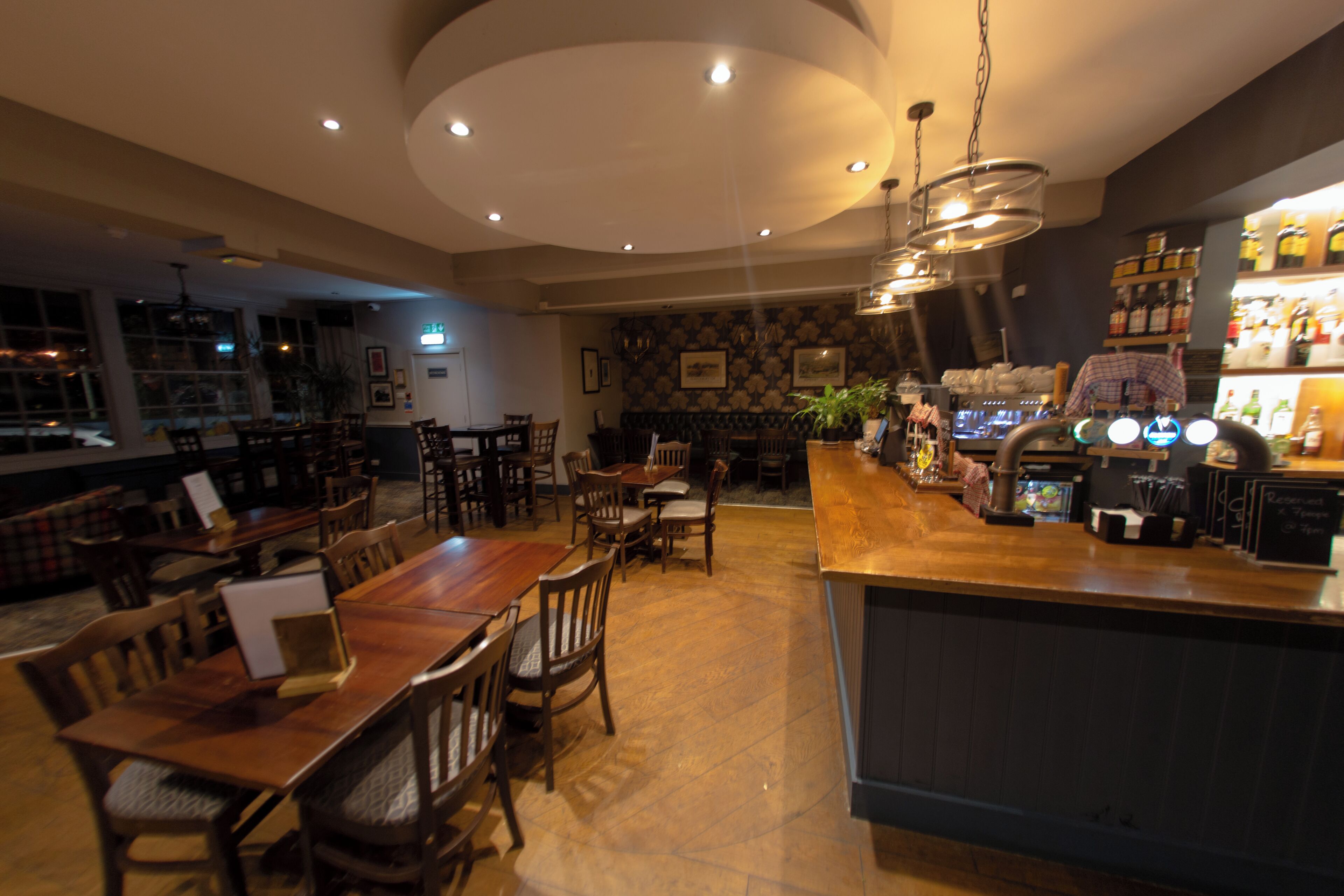 A restaurant with a bar area, wooden tables, and chairs.