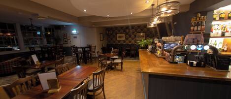A restaurant with a bar area, wooden tables, and chairs.