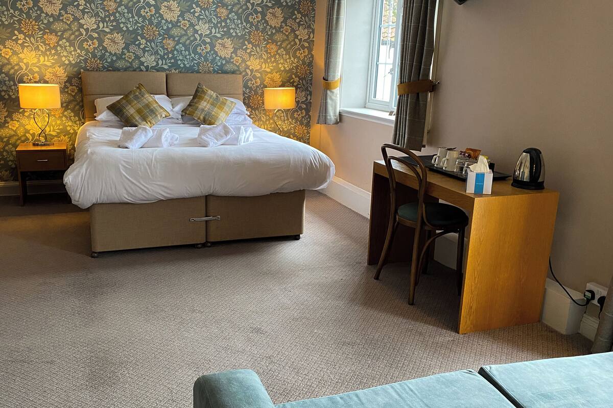 A hotel room with a bed, bedside lamps, a desk with a chair, and a window with curtains.