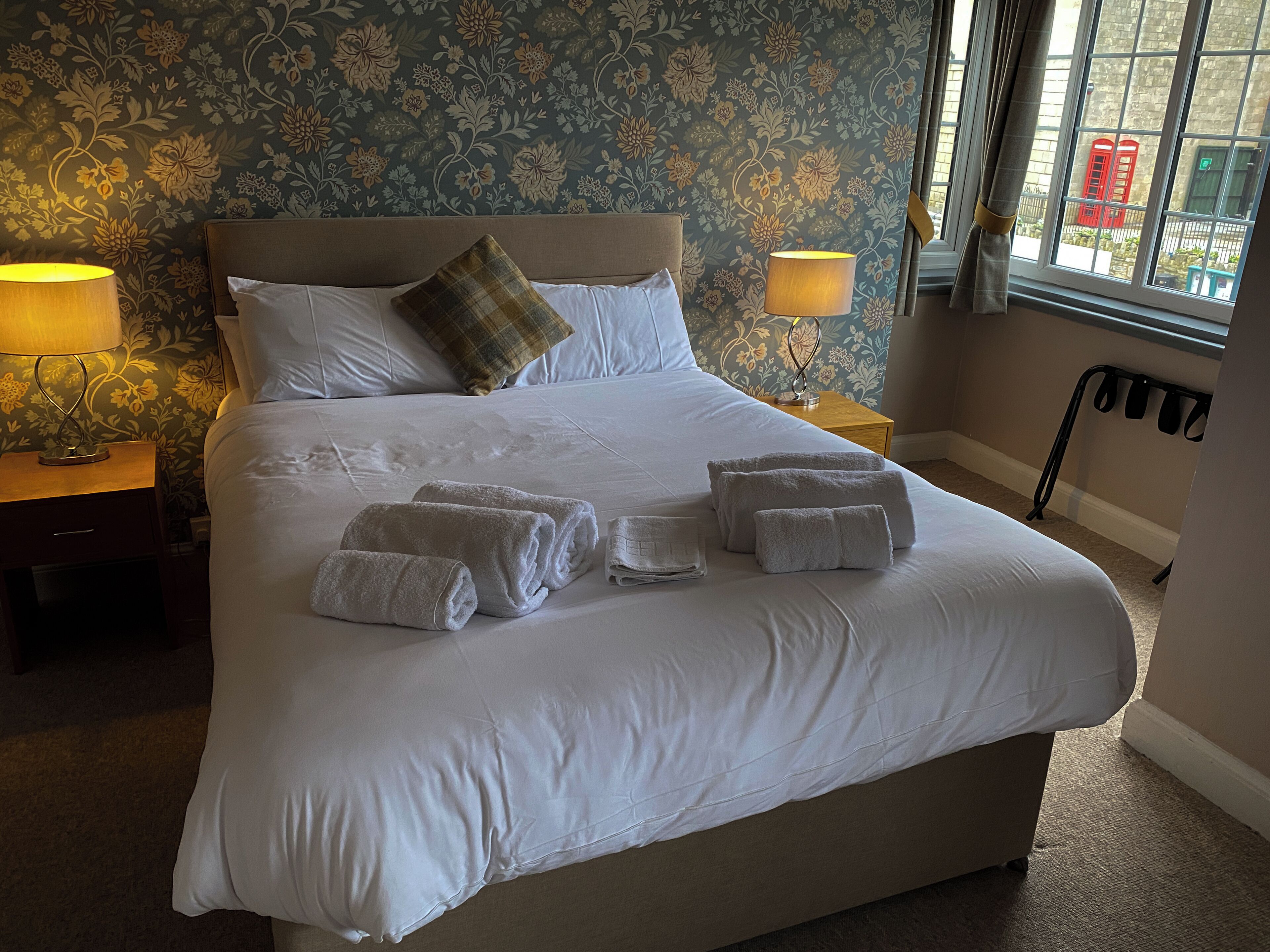 A neatly made bed with white linens, two bedside lamps, and a floral wallpaper pattern.