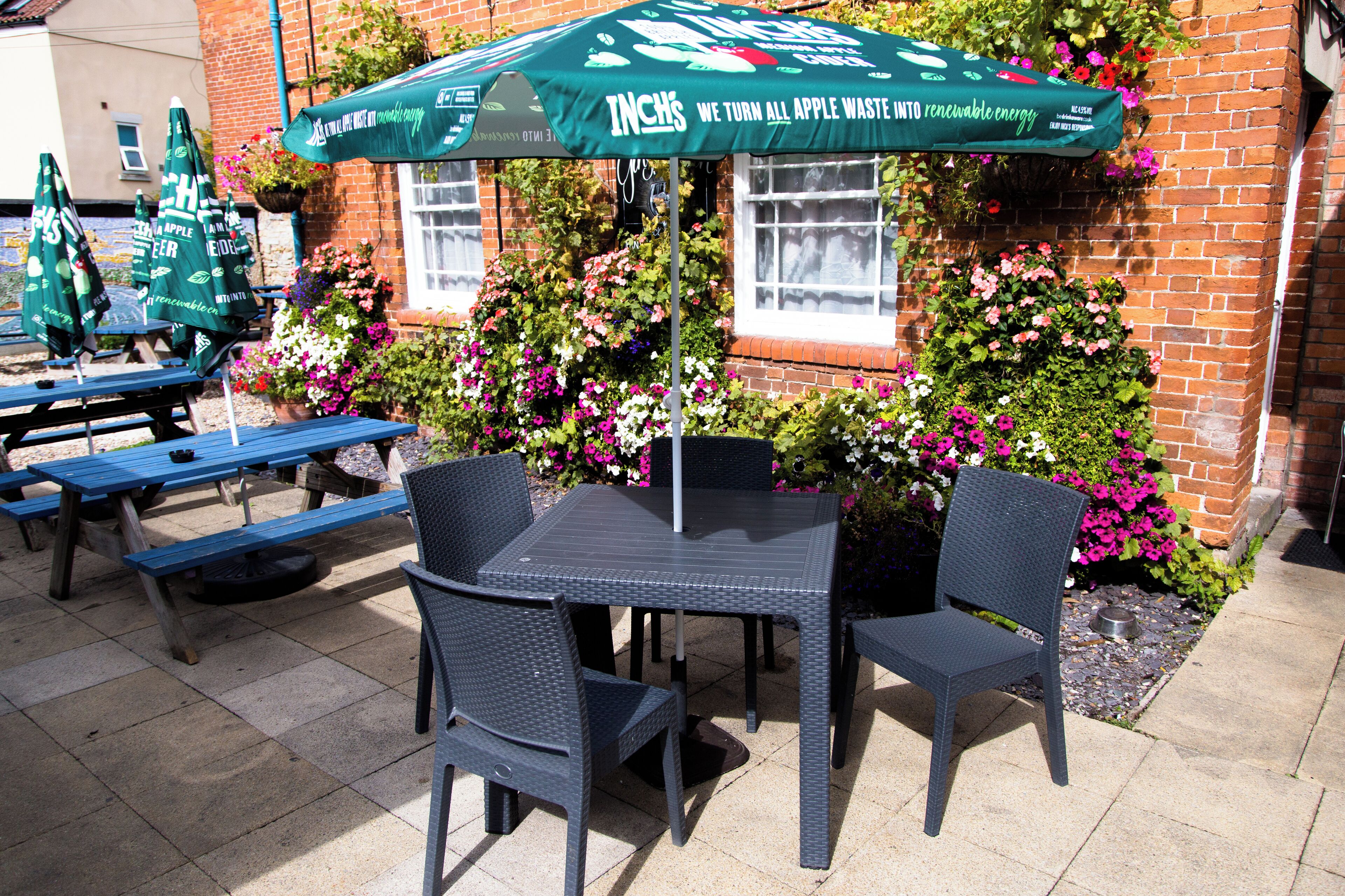 Un espace extérieur aménagé avec une table et des chaises, un parasol vert et des jardinières fixées à la façade du bâtiment.