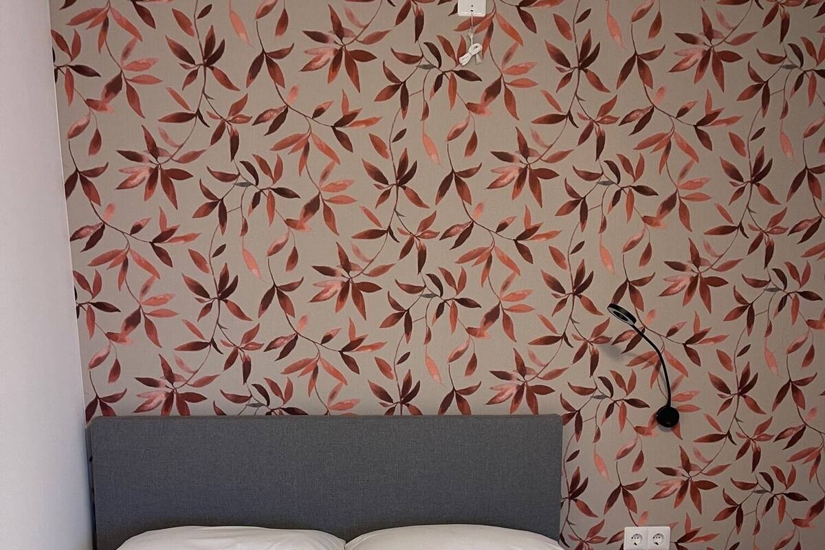 A neatly made bed with white bedding, a grey headboard, and a wall with a leaf pattern.