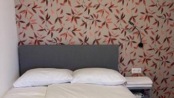 Una cama bien hecha con ropa de cama blanca, un cabecero gris y una pared con un diseño de hojas.