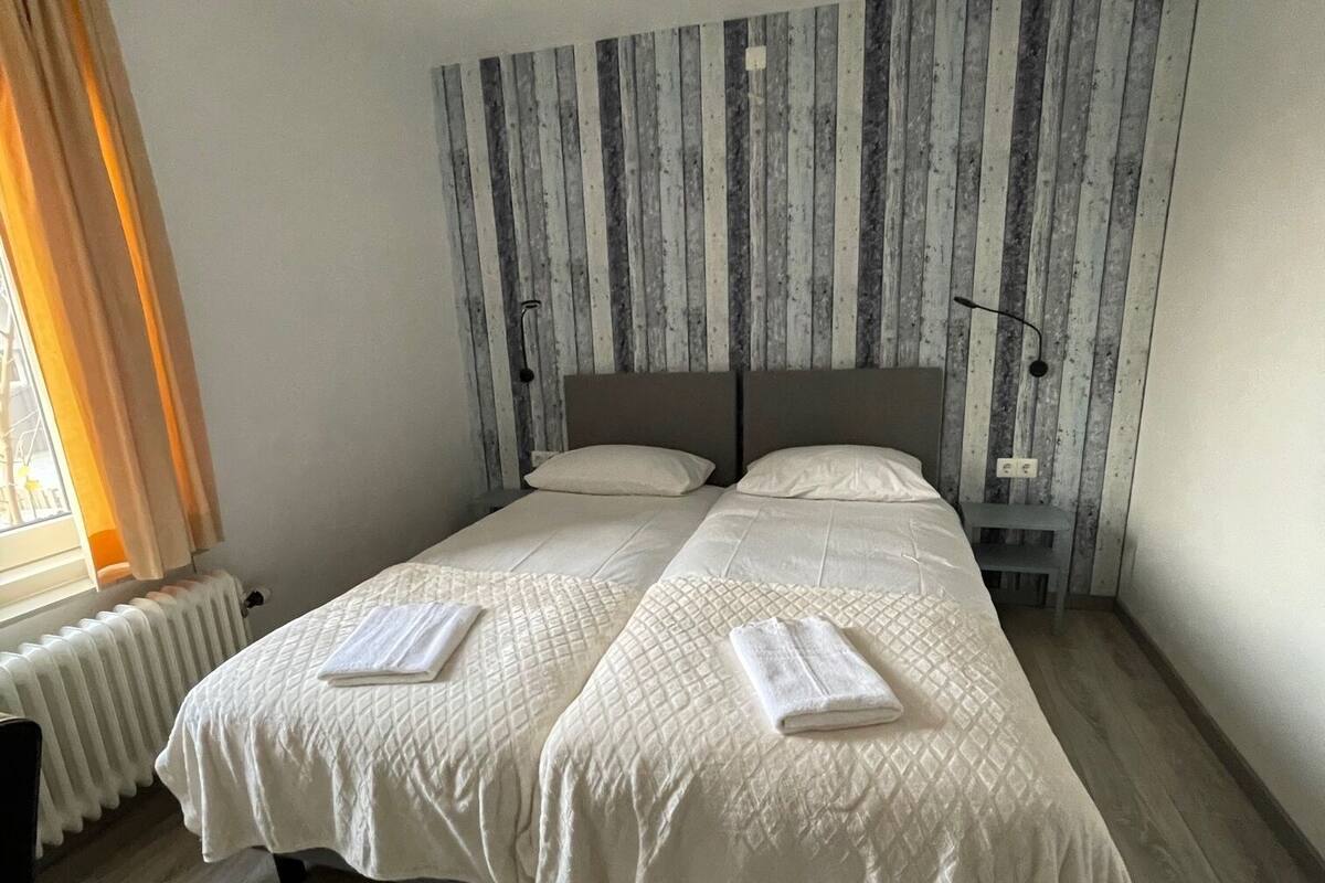 A double bed with two pillows and a blanket, a ceiling fan, a radiator, and a striped wall.