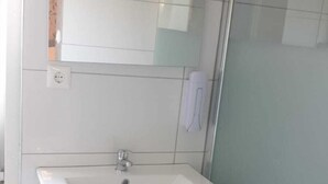 Ein Badezimmer mit einem weißen Waschbecken, einem Spiegel und einer Duschkabine.