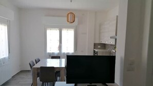 A modern living room with a flat-screen TV, a dining table with chairs, and a kitchen area with cabinets. - Very central and airy apartment in Palau (Palau)
