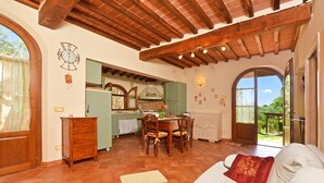 A spacious living room with a wooden ceiling, a dining area with a table and chairs, a kitchen with green cabinets, and a large arched window. - Da Maria (Murlo)