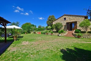 Une maison en pierre avec un jardin, une zone pavée et un espace salon abrité.