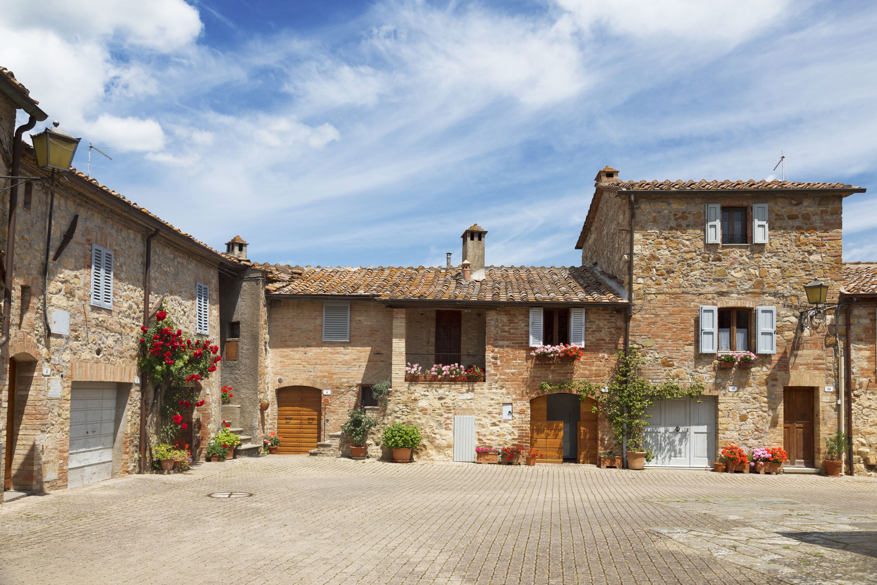 A stone building with a tiled roof, a central courtyard, and flower boxes on the windows.
