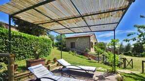 A covered outdoor area with two lounge chairs, a wooden deck, and a stone building in the background. - Da Maria (Murlo)