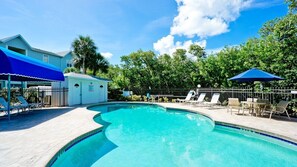 Une piscine entourée d’une clôture et d’arbres, avec des chaises longues et des parasols.
