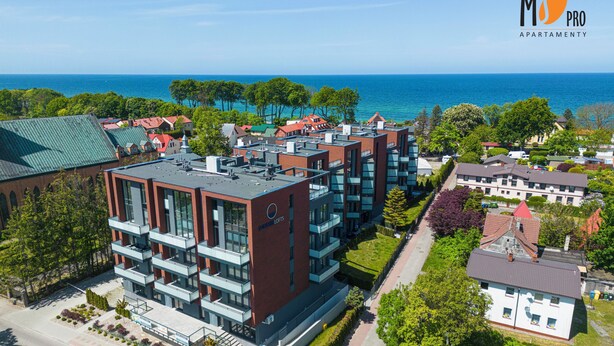 A modern apartment complex with multiple buildings, a well-maintained lawn, and a view of the sea. - SUMMER LOFTS Apartamenty Premium (Ustronie Morskie)
