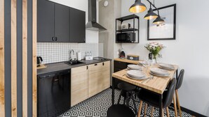 A modern kitchen with black cabinets, a wooden countertop, and a dining area with a wooden table and chairs. - SUMMER LOFTS Apartamenty Premium (Ustronie Morskie)