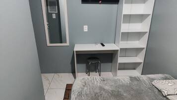 Una habitación con cama, escritorio, silla, televisor y estantería.